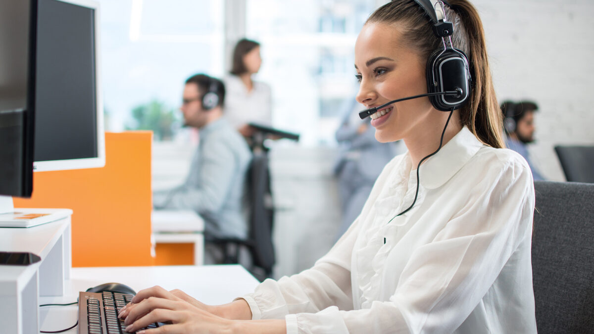 Friendly customer support operator with headset and microphone assisting to client in call centre