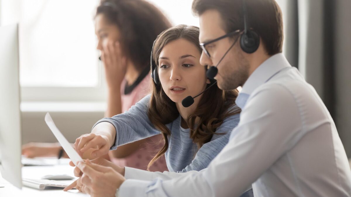 Call center agents in headsets discussing papers helping at workplace